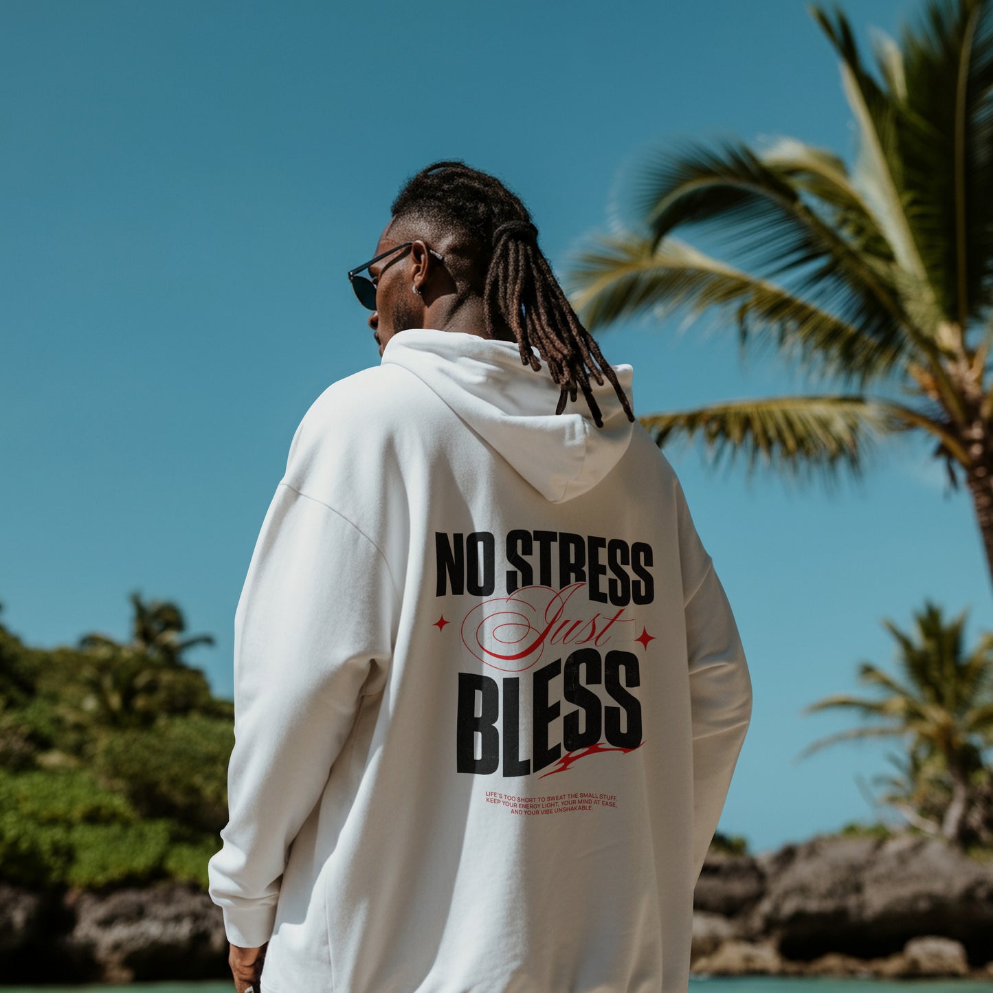 Person wearing a white hoodie with 'No Stress Just Bless' text, standing by a tropical beach.